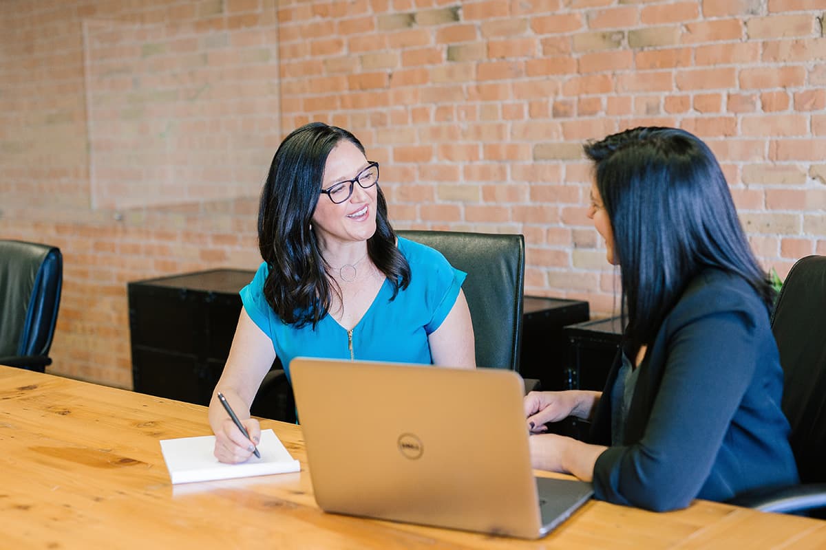 Two women discussing with laptop and paper.