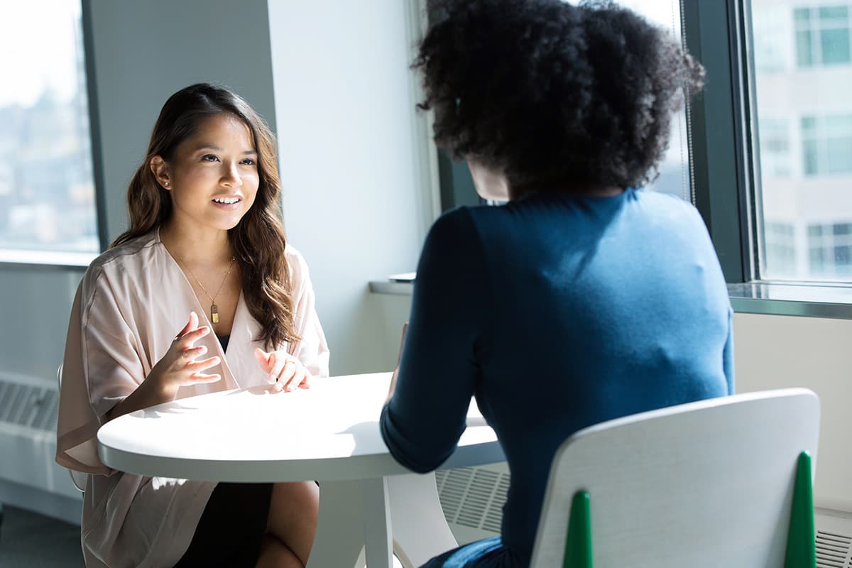 Two women discussing by the table in front of a window.