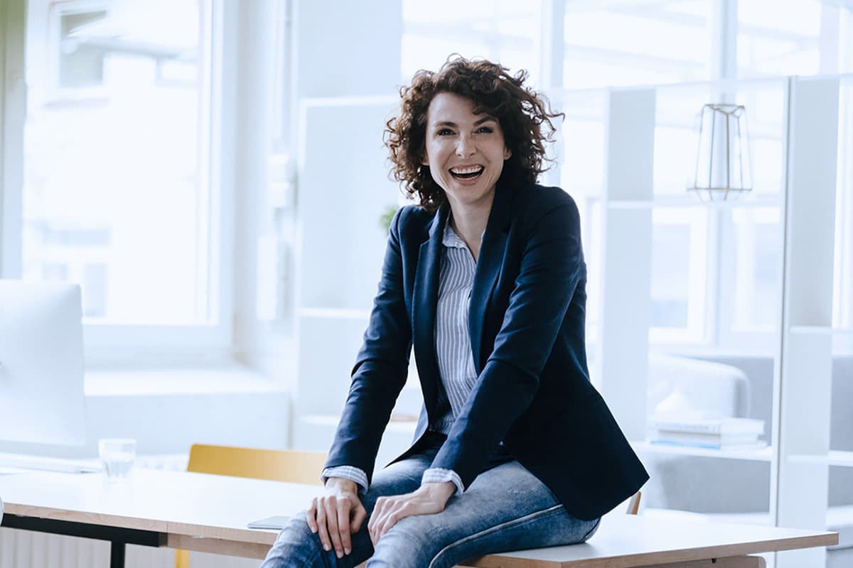 Iloinen nainen istuu pöydällä toimistossa.