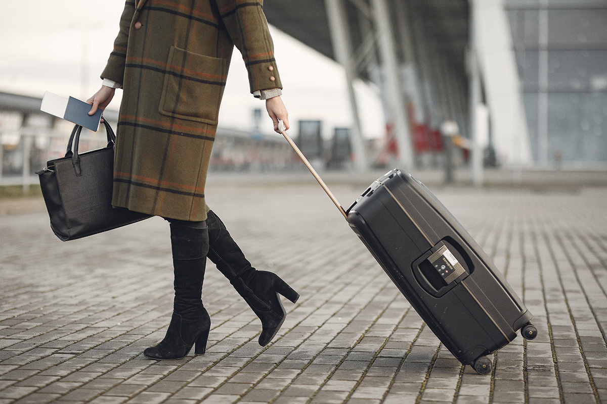 Woman carrying a hand bag and pulling luggage.