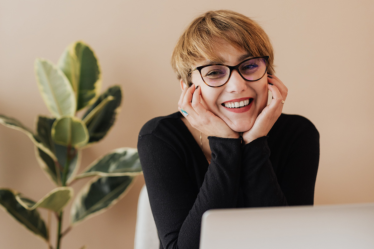 Woman with glasses smiling behind a laptop.